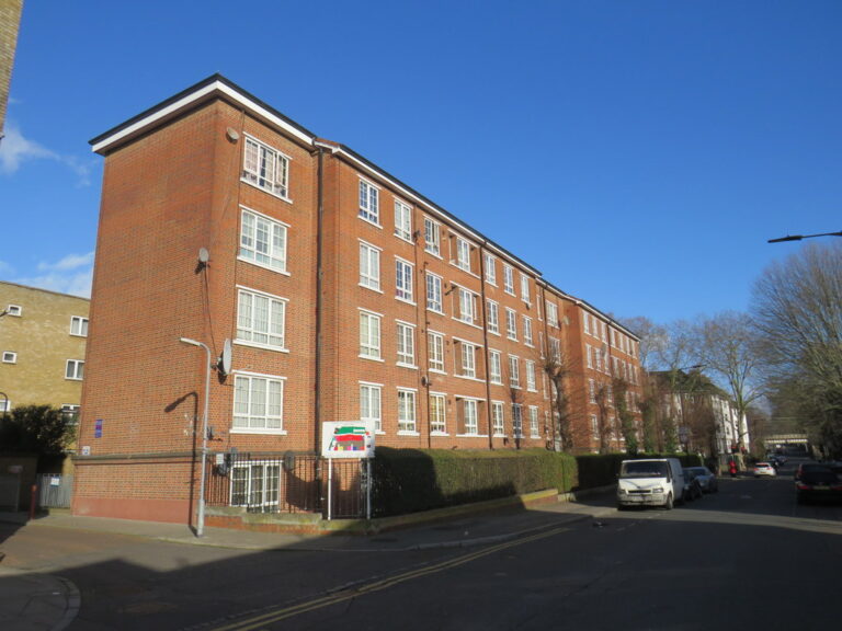 A row of red-brick housing association flats beside a street in Hackney.