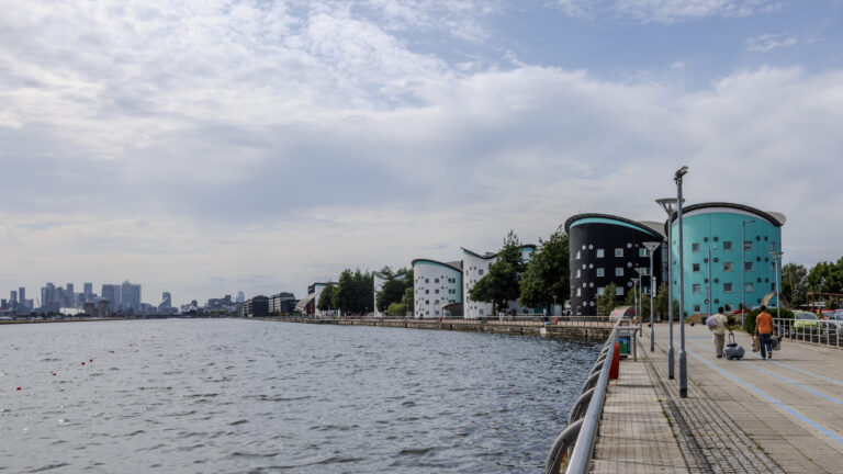 Campus buildings and a waterside path beside Royal Albert Dock.