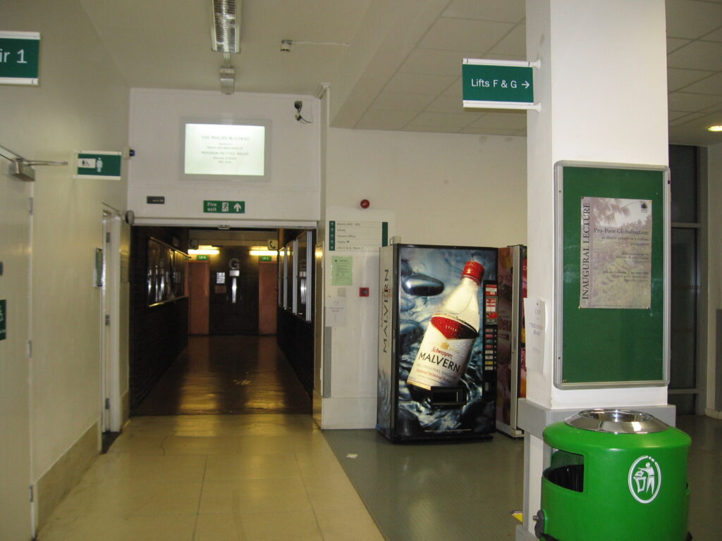 University complaint guide: SOAS interior corridor with lift signs and a vending machine, shown for context